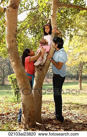 Stock Image - Family at park, daughter up tree. Fotosearch