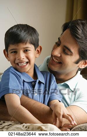 father hugging son on couch, son smiles at camera View Large Photo Image Picture - father hugging son on couch, son smiles at camera. Fotosearch