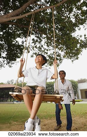 Picture - father pushing son in swing. Fotosearch