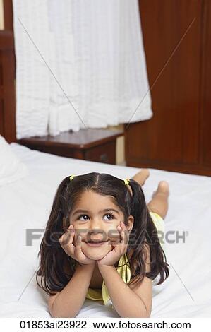 Stock Image - Girl on bed, resting chin in hands. Fotosearch