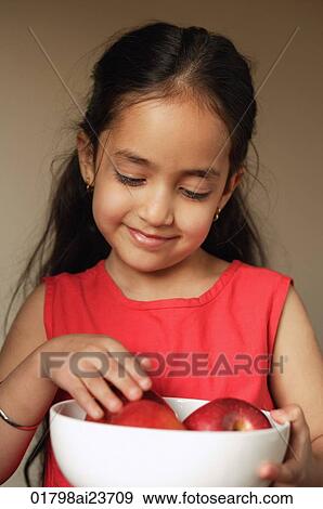 Stock Photo - little girl holding bowl of apples, eyes down. Fotosearch