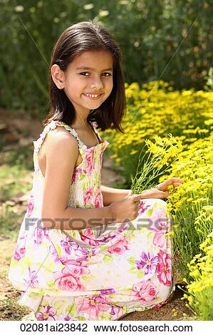 Stock Image - Little girl kneeling by yellow flowers. Fotosearch