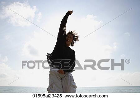 Man at beach jumping in the air with arm raised View Large Photo Image Stock Photography - Man at beach jumping in the air with arm raised. Fotosearch