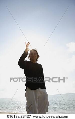 Stock Photo - Man raising hand at the beach, looking at camera. Fotosearch