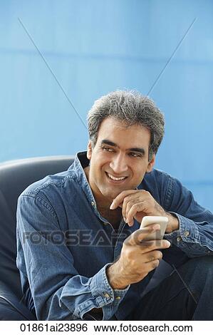 Stock Photograph - Man with gray hair, hand on chin, holding phone. Fotosearch