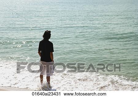 Man with legs in water looking out to sea at the beach View Large Photo Image Stock Image - Man with legs in water looking out to sea at the beach. Fotosearch