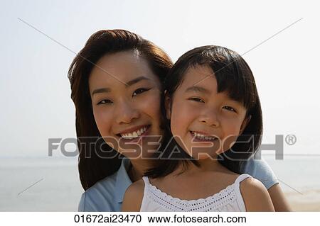 Stock Image - Mother and daughter at the beach, smiling at camera. Fotosearch