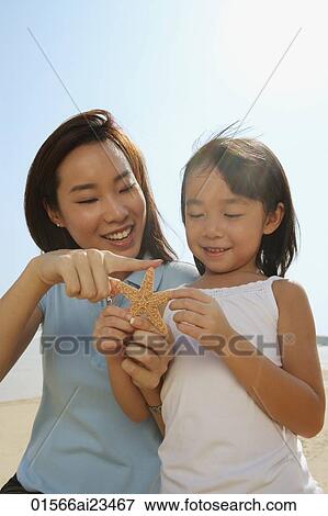 Mother and daughter at the beach, looking at shell View Large Photo Image Stock Photo - Mother and daughter at the beach, looking at shell. Fotosearch