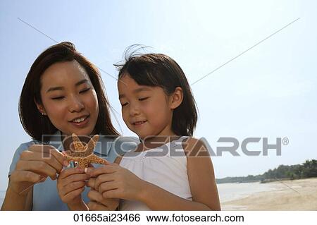 Stock Photograph - Mother and daughter at the beach, looking at shell. Fotosearch