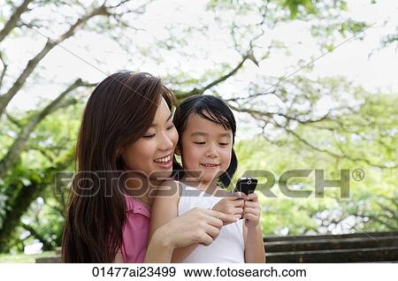 Stock Photo - Mother and daughter at the park looking at cellphone. Fotosearch
