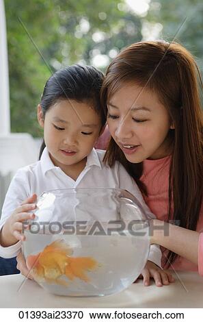 Stock Image - Mother and daughter looking at goldfish bowl. Fotosearch