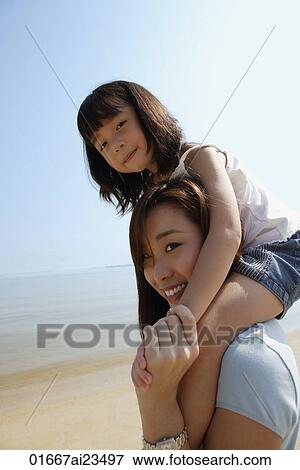 Mother carrying daughter on her shoulders at the beach, both looking at camera View Large Photo Image Stock Photo - Mother carrying daughter on her shoulders at the beach, both looking at camera. Fotosearch