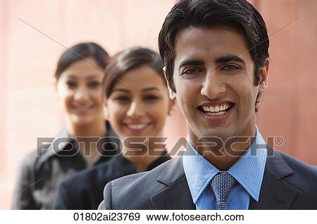 Stock Photo - one businessman in foreground, two businesswomen in background, all smiling (horizontal). Fotosearch