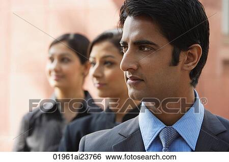 Stock Photograph - one businessman in foreground, two businesswomen in background (horizontal). Fotosearch
