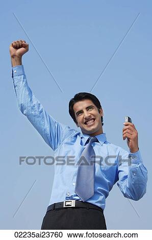 Stock Image - smiling business man with fist in air, phone in hand. Fotosearch