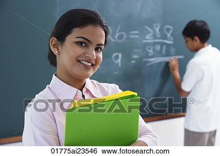 Stock Photograph - smiling teacher holding notebooks, boy at chalkboard. Fotosearch