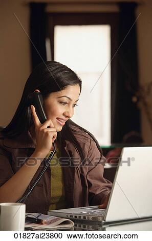 Stock Image - smiling woman working at laptop on phone. Fotosearch