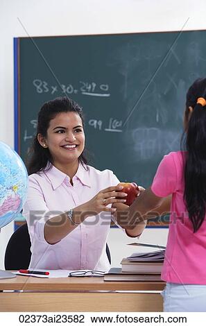 Stock Image - student handing apple to teacher. Fotosearch