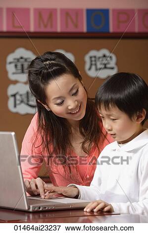 Teacher helping student use a laptop in class View Large Photo Image Stock Photo - Teacher helping student use a laptop in class. Fotosearch