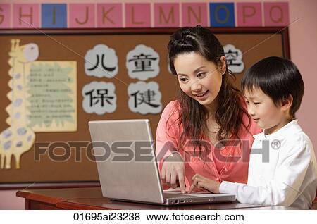 Stock Photo - Teacher helping student use a laptop in class. Fotosearch