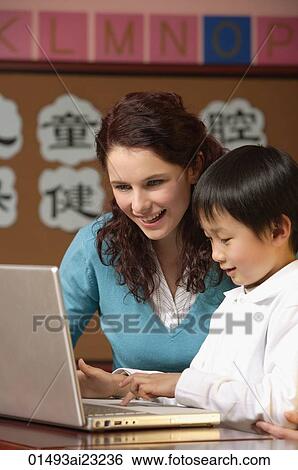 Teacher helping student use a laptop in class View Large Photo Image Stock Photograph - Teacher helping student use a laptop in class. Fotosearch