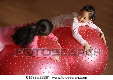 Stock Image - Two girls leaning on balls, looking at each other. Fotosearch
