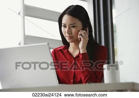 Picture - woman working at laptop, talking on phone. Fotosearch
