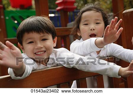 Stock Image - Young boy and girl at playground, waving and looking at camera. Fotosearch