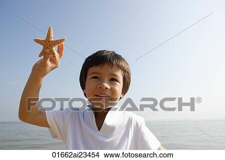 Young boy holding shell at the beach View Large Photo Image Picture - Young boy holding shell at the beach. Fotosearch