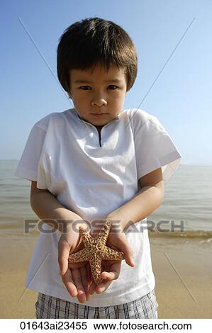 Young boy holding shell on both hands at the beach, looking at camera View Large Photo Image Stock Photography - Young boy holding shell on both hands at the beach, looking at camera. Fotosearch