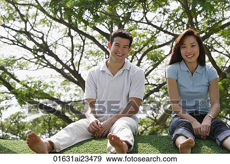 Young couple sitting on ground at the park, looking at camera View Large Photo Image Stock Photo - Young couple sitting on ground at the park, looking at camera. Fotosearch