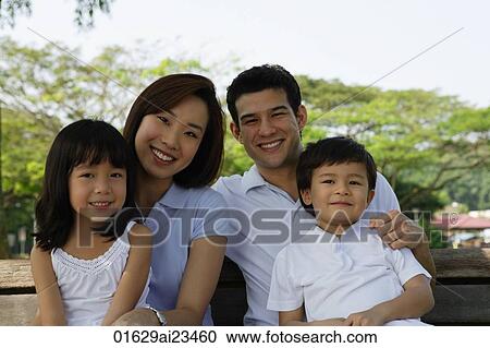 Stock Image - Young family sitting on park bench. Fotosearch