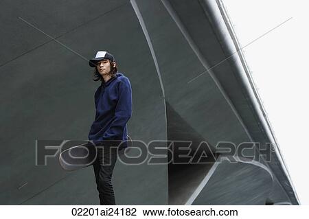 Stock Image - young man with skateboard, wearing cap. Fotosearch