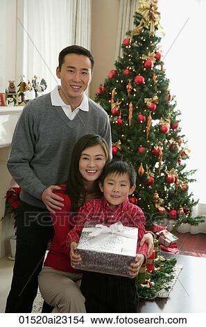 Young parents with boy present in hand at Christmas smiling at camera View Large Photo Image Picture - Young parents with boy present in hand at Christmas smiling at camera. Fotosearch