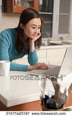 Young woman using laptop on kitchen top View Large Photo Image Stock Photo - Young woman using laptop on kitchen top. Fotosearch