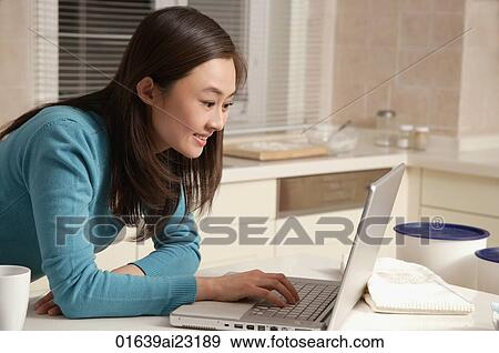 Young woman using laptop on kitchen top View Large Photo Image Stock Photo - Young woman using laptop on kitchen top. Fotosearch