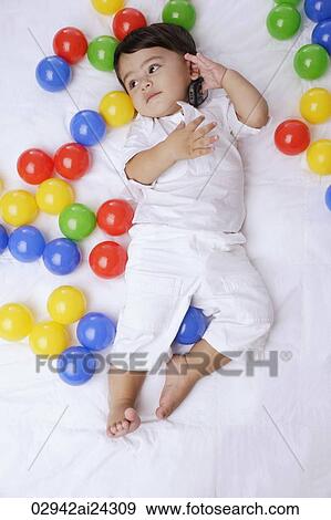 Stock Photo - baby boy surrounded by balls, cell phone to ear. Fotosearch