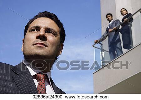 Stock Image - businessman in foreground, business associates looking down from balcony. Fotosearch