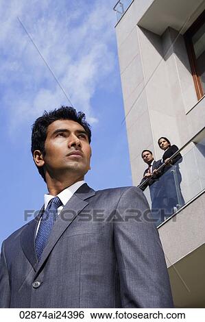 Stock Photograph - businessman in foreground, business associates looking down from balcony. Fotosearch