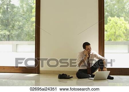 Stock Image - businessman on phone, sitting on ground with computer. Fotosearch