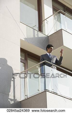 Stock Photo - businessman with mobile phone standing on balcony. Fotosearch