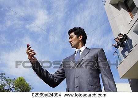 Picture - businessman with phone, associates on balcony above. Fotosearch