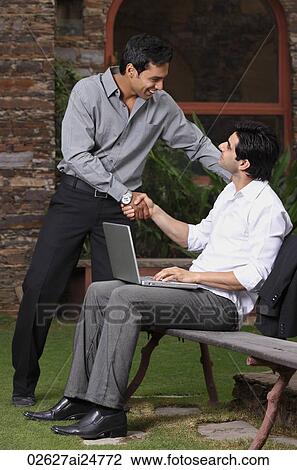 Stock Image - businessmen shaking, one at laptop computer. Fotosearch