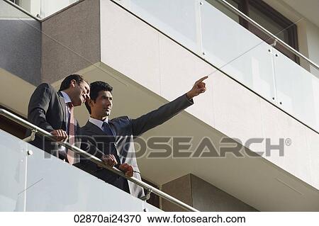 Stock Image - businessmen standing on balcony, one pointing to distance. Fotosearch
