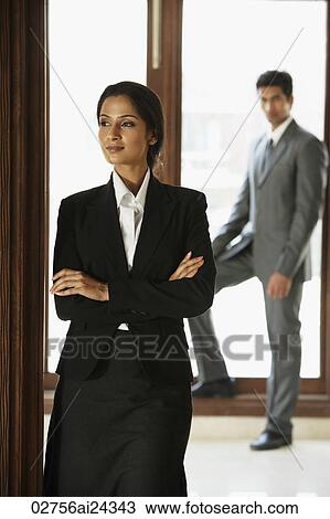 Stock Image - businesswoman with folded arms in foreground, businessman in background. Fotosearch
