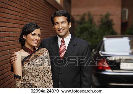 Stock Image - couple in front of car, woman in sari. Fotosearch