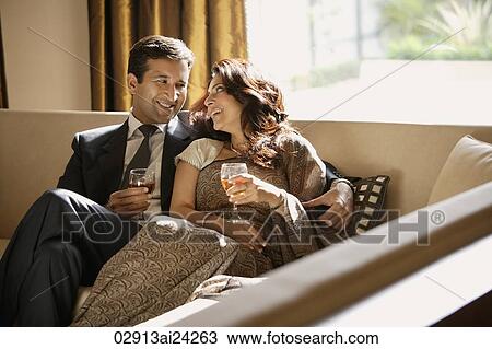 Stock Image - couple on couch, smiling at each other, holding wine glasses. Fotosearch
