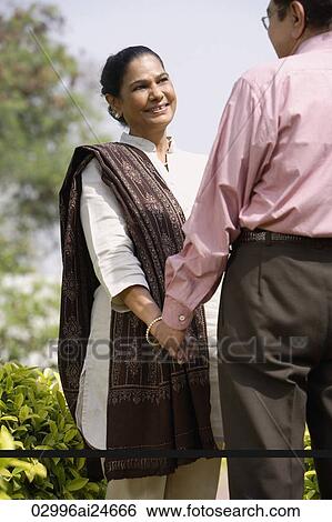 Stock Photograph - couple outdoors holding hands, woman wearing salwar kameez and shawl, smiling at man. Fotosearch