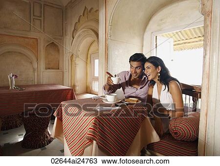 Stock Image - couple sitting at table, man pointing out. Fotosearch