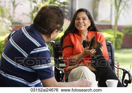 Stock Photograph - couple sitting outdoors, playing with dog. Fotosearch